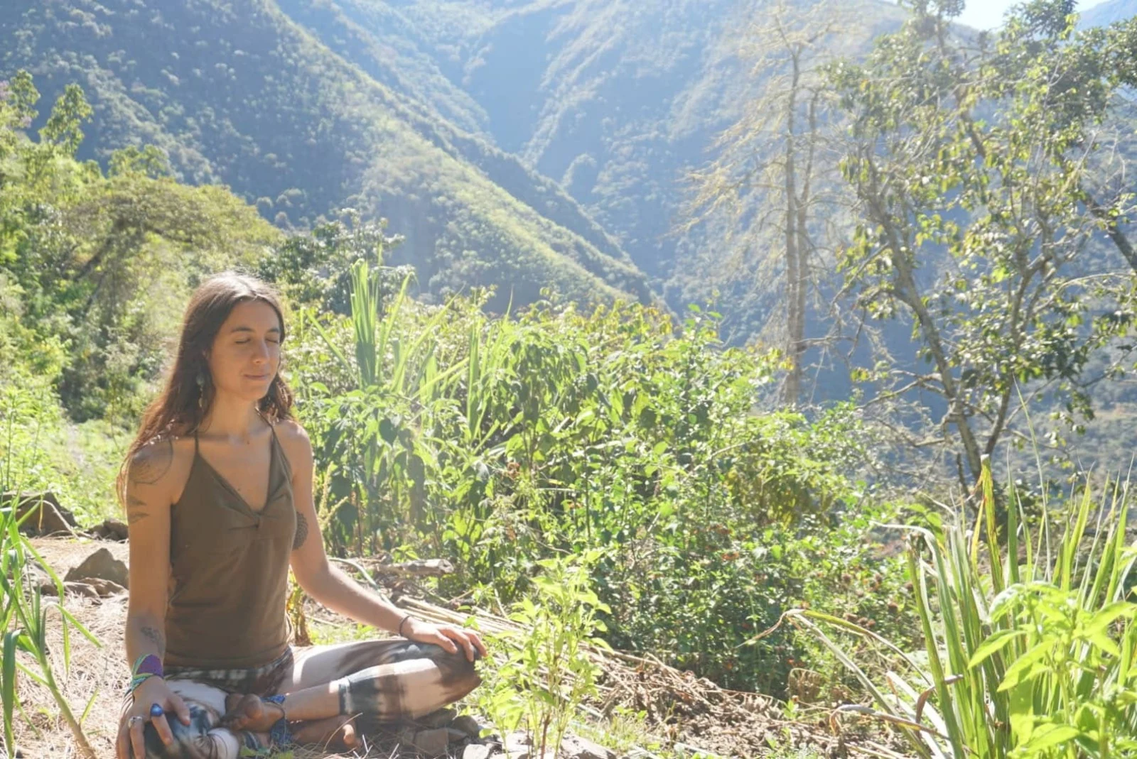 Una mujer sentada en meditación en un claro de la ladera, sobre el valle boscoso