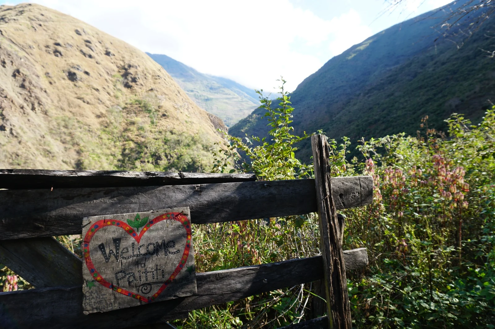 Un corazón de madera pintado a mano con la leyenda &ldquo;Welcome to Paititi&rdquo; en el portón de entrada a la reserva, con el valle del Mapacho al fondo